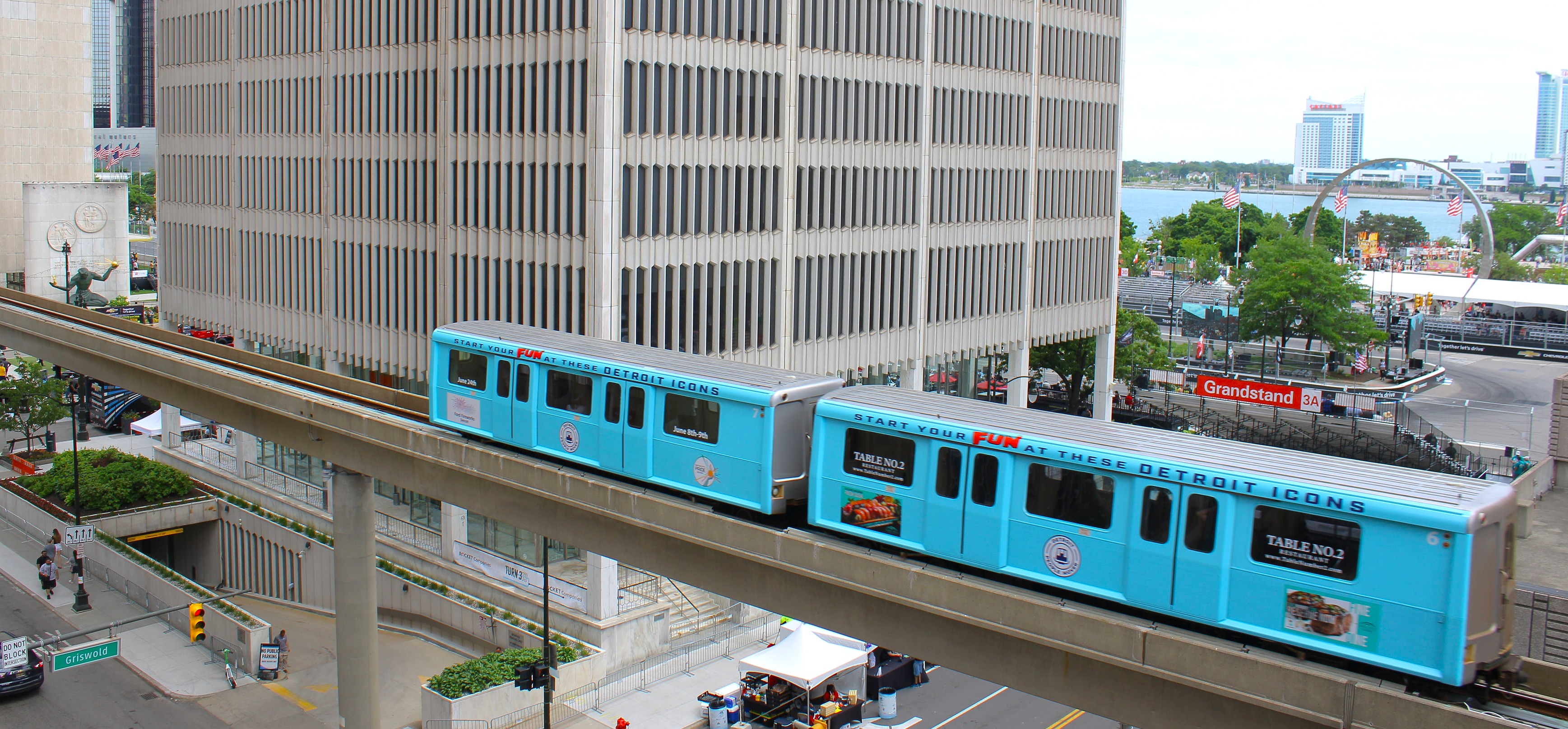 A blue Detroit People Mover train traveling above downtown near the Detroit River
